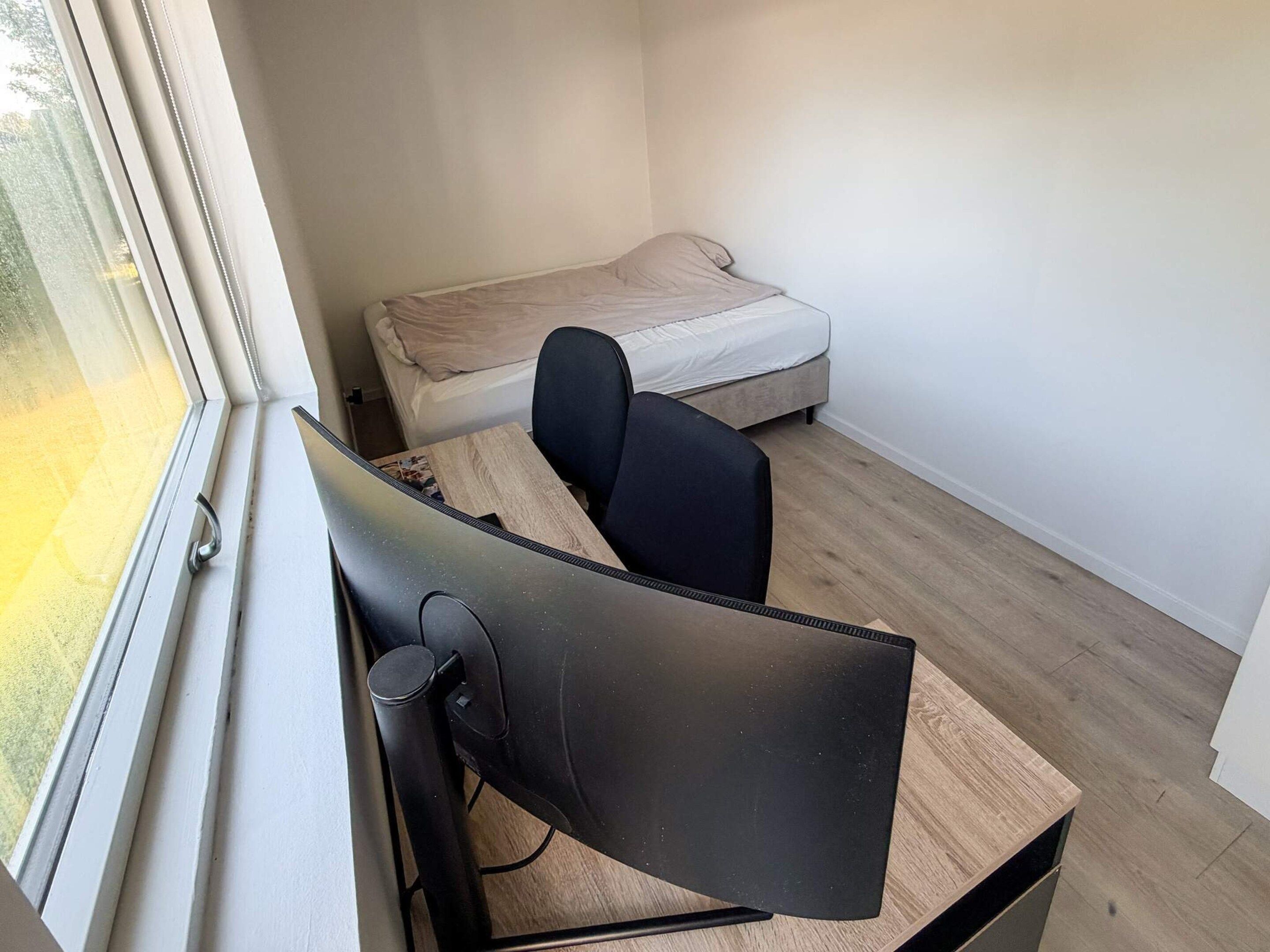 A bedroom with a single bed, a desk with a computer, and a window.