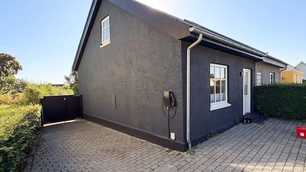 Uma casa moderna com fachada escura, porta de garagem e entrada pavimentada.