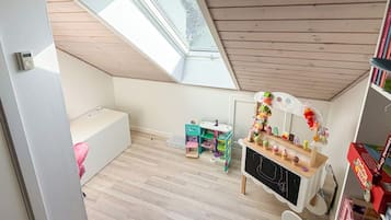 A room with a sloped ceiling, a skylight, a play area with a small table and chairs, and a bookshelf.