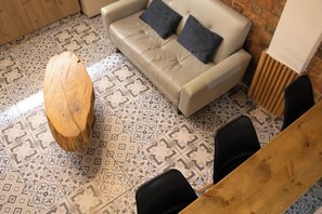Una stanza con pavimento decorato, un divano con cuscini, un tavolo di legno e una sedia.