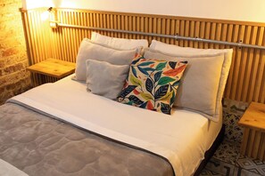 Un letto con copriletto trapuntato, due cuscini e un cuscino decorato con motivi a foglie colorate. Sono presenti una testiera e dei comodini in legno con lampade.