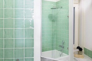 Une salle de bain avec des carreaux verts, une douche à l’italienne et une baignoire.