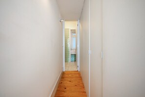 A narrow hallway with wooden flooring leading to a bathroom with a green tiled wall and a white door. - GuestReady - Striking apt near Santa Justa Lift (Lisbon)