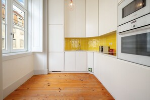 A kitchen with white cabinets, a yellow backsplash, and wooden flooring. - GuestReady - Striking apt near Santa Justa Lift (Lisbon)
