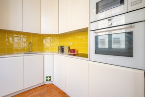 Une cuisine avec des meubles blancs, un pare-feu jaune et un four Bosch.