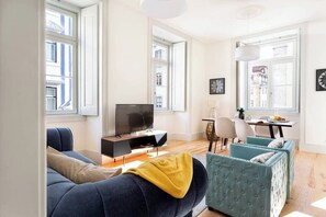 A living room with a sofa, a television, and a dining area with chairs and a table. - GuestReady - Striking apt near Santa Justa Lift (Lisbon)