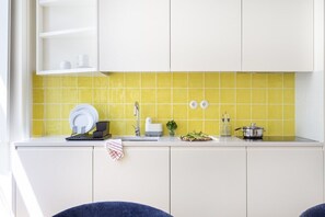 Une cuisine avec des meubles blancs, un pare-feu jaune et un évier avec un robinet.
