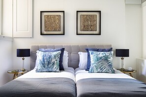 A double bed with a grey headboard, two side tables with lamps, and two framed artworks on the wall. - GuestReady - Great flat near Carmo Convent (Lisbon)