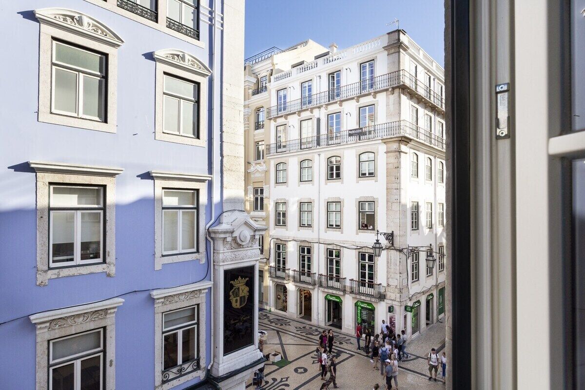 Une vue d’une rue bordée d’immeubles, avec une foule de personnes et un ciel dégagé.