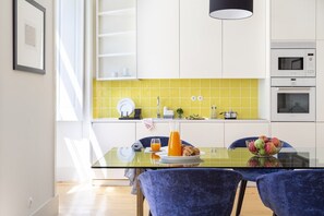 Eine moderne Küche mit weißen Schränken, einer gelben Spritzschutzleiste und einem Glastisch mit Stühlen.