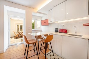 A modern kitchen with a white countertop, a red toaster, and a sink. There are two stools and a table with chairs. - GuestReady - Sleek home near the Botanical Garden (Lisbon)