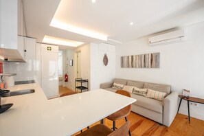 A modern kitchen with a white countertop, a dining table, and a sofa in the living area. - GuestReady - Sleek home near the Botanical Garden (Lisbon)