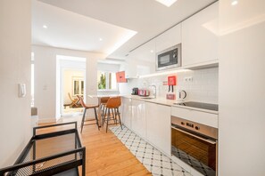 A modern kitchen with white cabinetry, a microwave, a toaster, and a coffee maker. - GuestReady - Sleek home near the Botanical Garden (Lisbon)