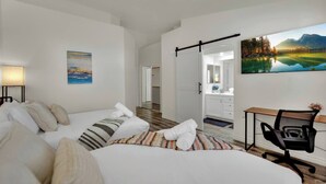A hotel room with two beds, a desk, a chair, a painting, and a view of a mountain landscape.