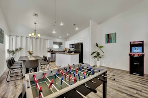 A modern kitchen with white cabinets, a dining area with a table and chairs, and a foosball table.