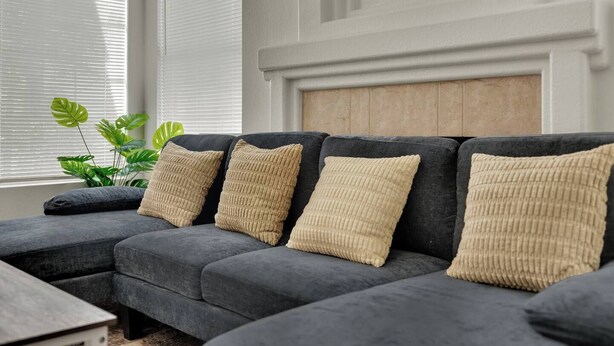 A sectional sofa with beige cushions, positioned in a room with a white wall and a wooden headboard.