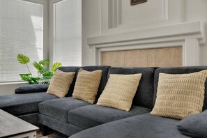 A sectional sofa with beige cushions, positioned in a room with a white wall and a wooden headboard.