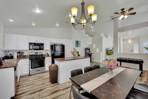 A modern kitchen with white cabinets, a granite countertop, a built-in oven, a black refrigerator, and a dining area with a marble table and chairs.