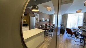 A modern kitchen with a central island, a dining area with a round table, and a living space with a sofa and a TV. - Undiscovered Gem in Rosebank 2BR (Johannesburg)