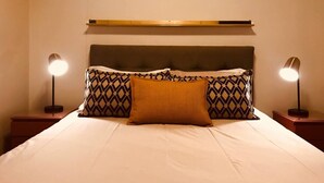 A bed with a headboard, two bedside lamps, and patterned pillows. - Undiscovered Gem in Rosebank 2BR (Johannesburg)