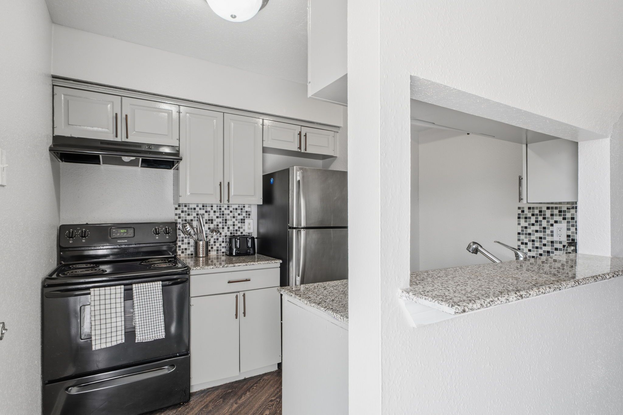 A modern kitchen with white cabinetry, a stainless steel refrigerator, a black stove, and a tiled backsplash.