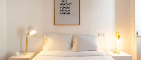 A hotel room with a bed, two bedside tables, two lamps, a wall-mounted light switch, and a framed sign with text.