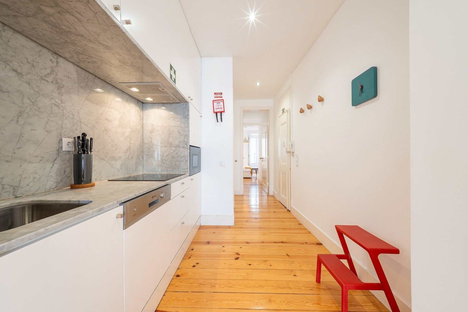 Una cocina moderna con salpicadero de mármol, suelo de madera y un banco rojo en un pasillo.