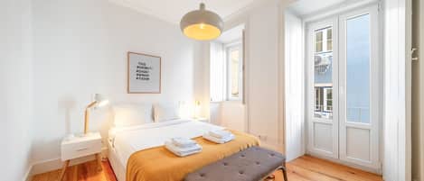 A hotel room with a bed, bedside table, lamp, bench, and a framed sign on the wall.