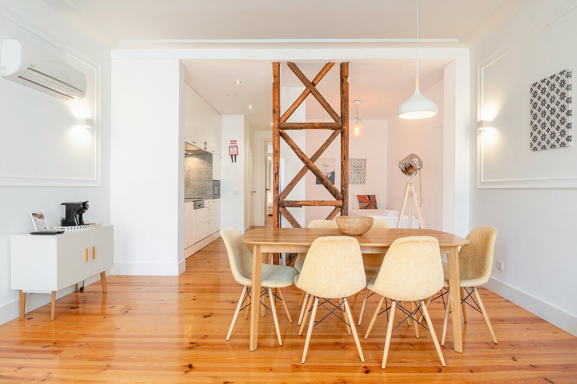 A dining area with a wooden table and chairs, a white cabinet with a coffee machine, and a wooden beam structure in the background.