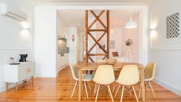 A dining area with a wooden table and chairs, a white cabinet with a coffee machine, and a wooden beam structure in the background.