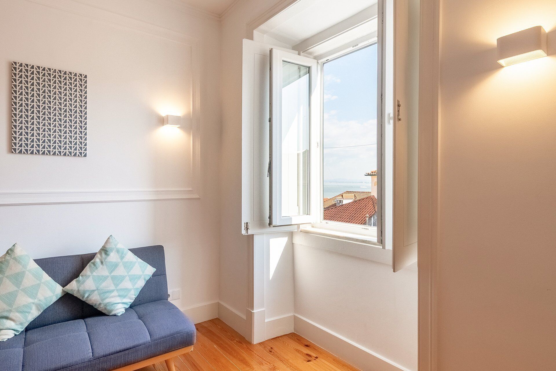 A room with a blue sofa, a patterned wall, a window with a view, and a light fixture.
