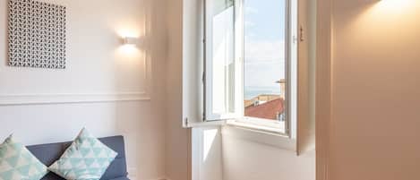 A room with a blue sofa, a patterned wall, a window with a view, and a light fixture.