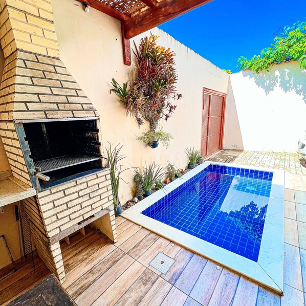 A backyard with a barbecue grill, a swimming pool, and potted plants. - Chalé tucano (Cunha)