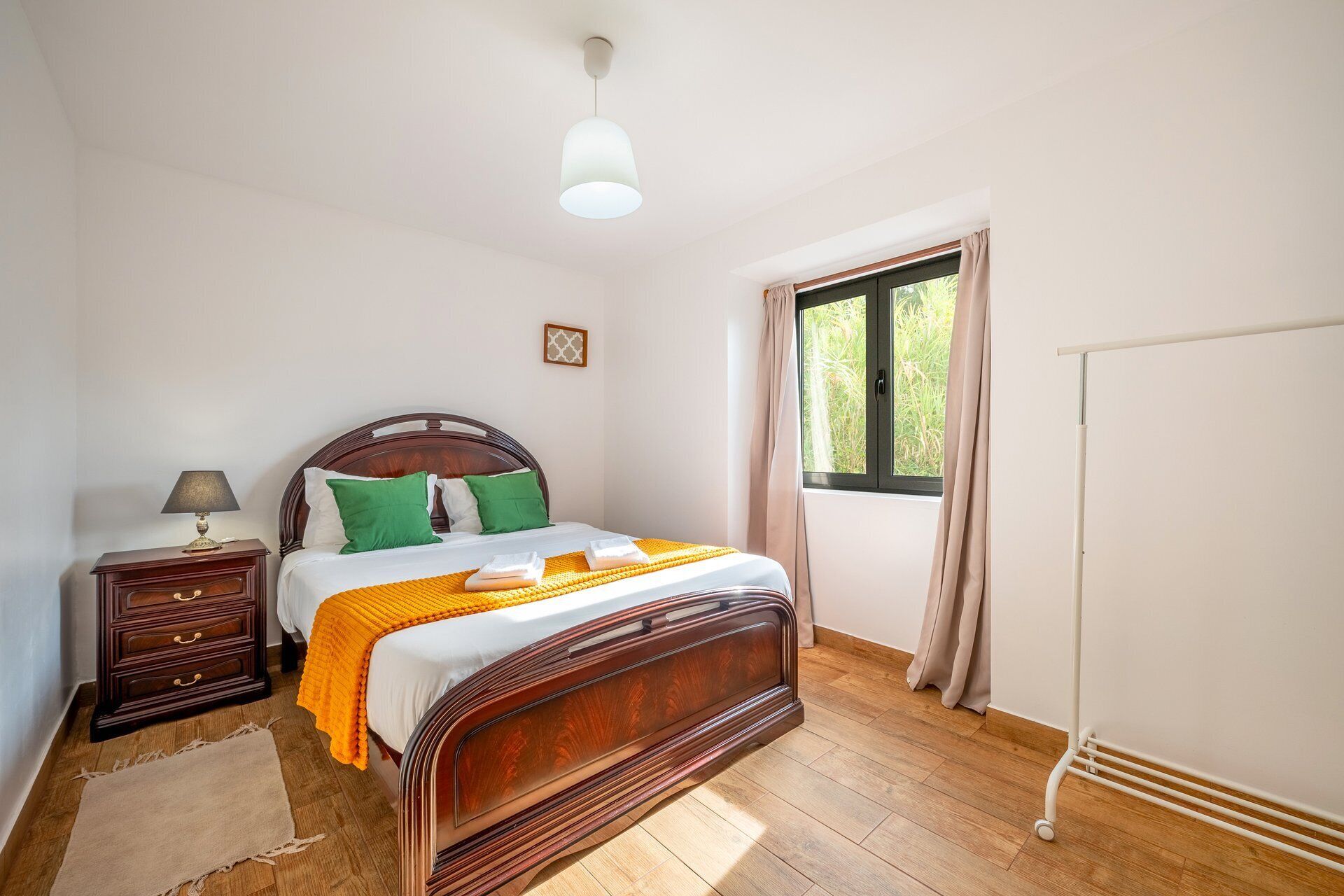Ein Schlafzimmer mit einem hölzernen Bett, einem Nachttisch mit Lampe, einem Fenster mit Vorhängen und einer Heizung.