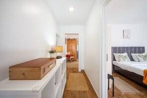 Ein Hotelzimmer mit einem Bett, einer Holzkommode, einem Schreibtisch mit Lampe und Blick auf den Flur.