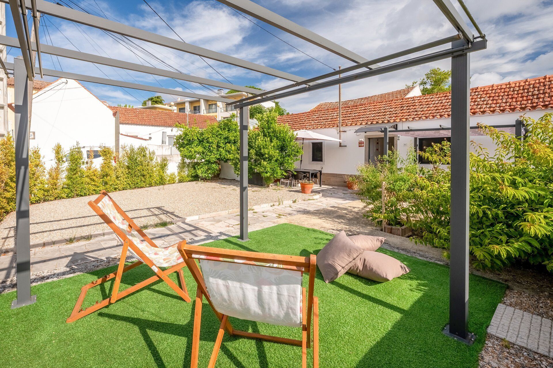 Un espacio al aire libre techado con césped artificial, un parque infantil con columpios y un patio con mesa y sillas.