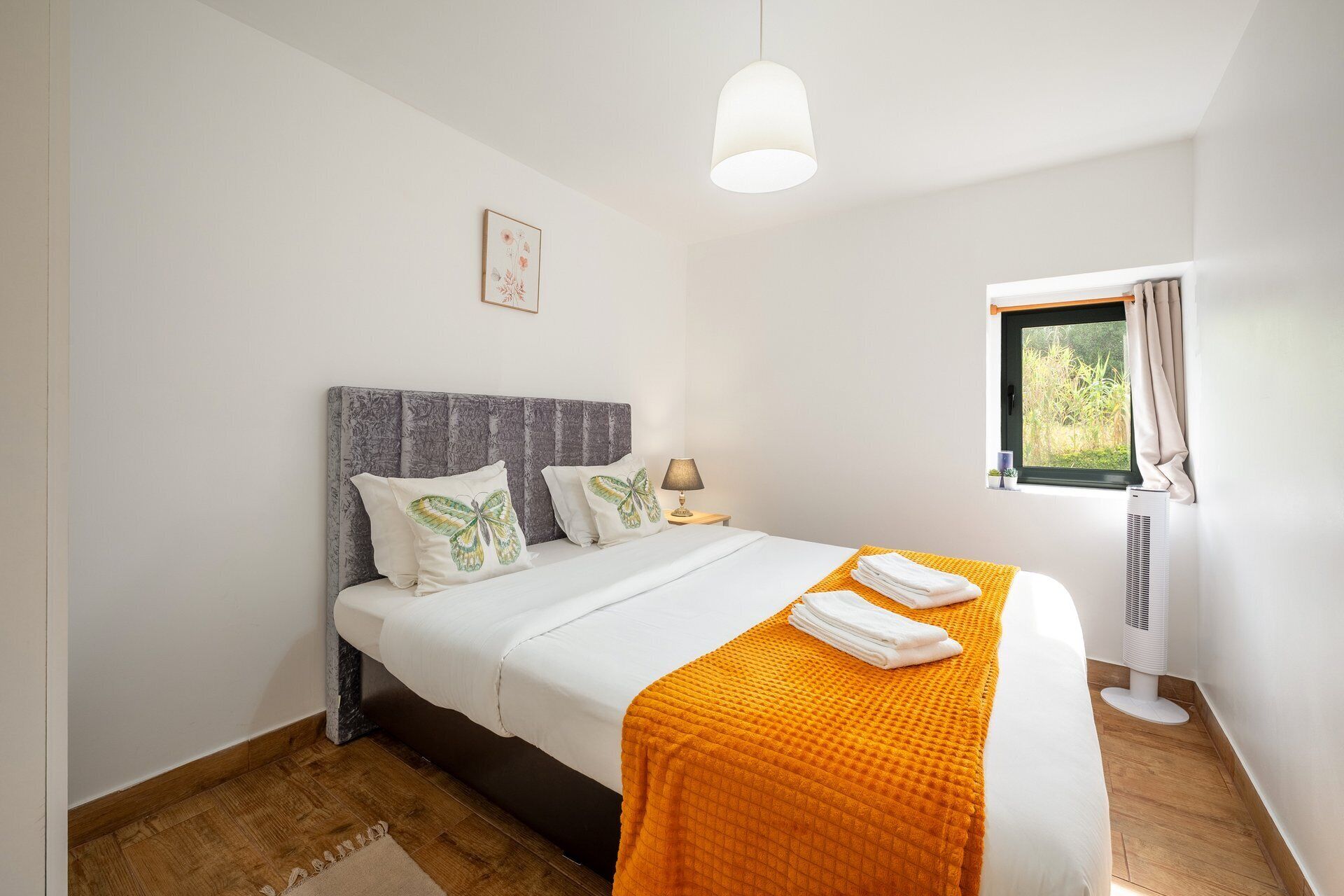 A bedroom with a bed, pillows, a bedside lamp, a window with curtains, and a wall-mounted air conditioner.