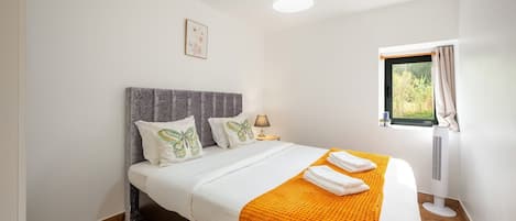 A bedroom with a bed, pillows, a bedside lamp, a window with curtains, and a wall-mounted air conditioner.