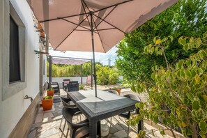 Eine Außenpatio mit Tisch und Stühlen, einer Pergola mit Dach und Kübelpflanzen.