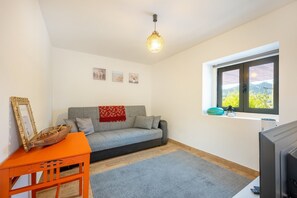 Ein gemütliches Wohnzimmer mit einem grauen Sofa, einem kleinen orangefarbenen Tisch und einem Fernseher.