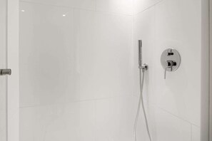Eine moderne Dusche mit chromfarbenem Wasserhahn und Bedienfeld, vor einer schlicht gefliesten Wand.