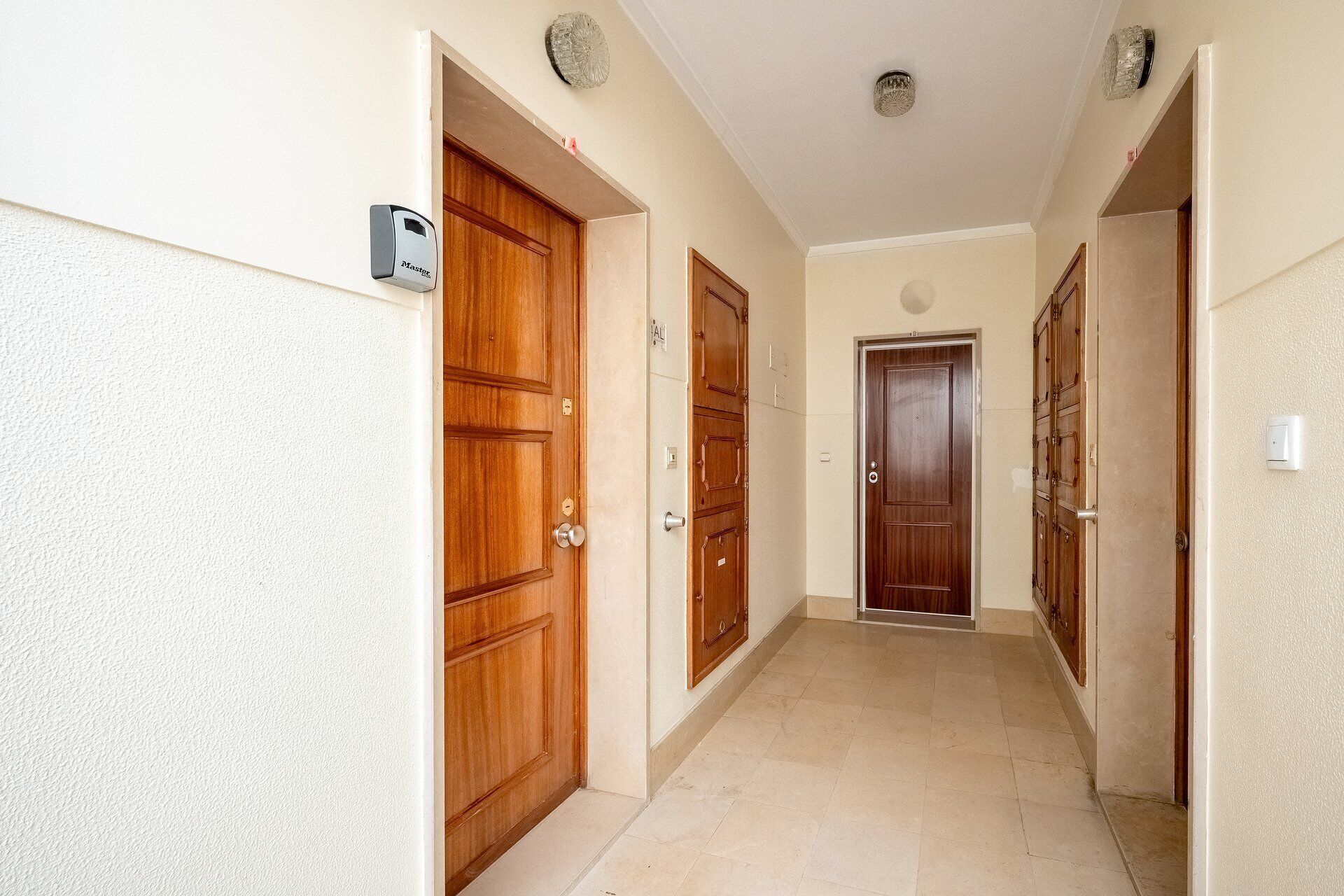 A hallway with wooden doors and a light switch on the wall.