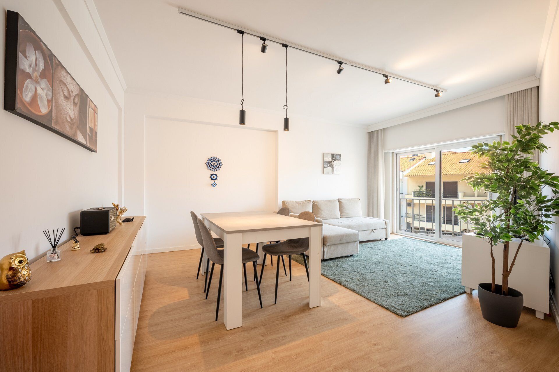A modern living space with a dining area, a sofa, a large window, and a potted plant.