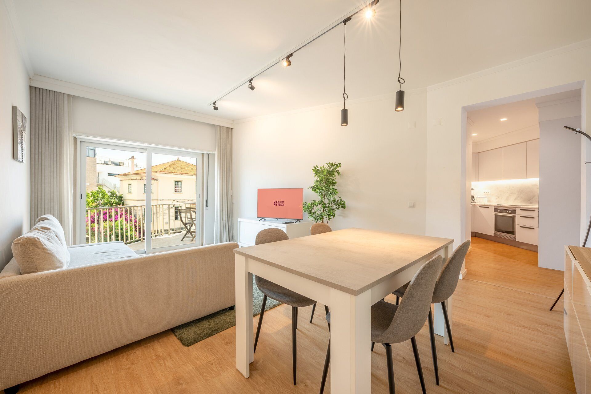 Un salon moderne avec un canapé, une table à manger et des chaises. Il y a un téléviseur accroché au mur et une plante posée sur la table.