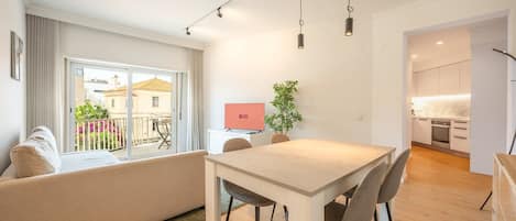 Uma sala de estar moderna com sofá, mesa de jantar e cadeiras. Há uma televisão na parede e uma planta na mesa.