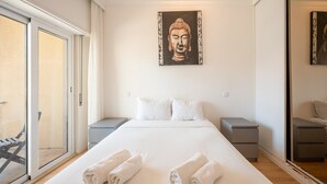 Habitación de hotel con una cama grande, dos mesitas de noche, un cuadro en la pared y un ventanal corredero que da a un espacio exterior.