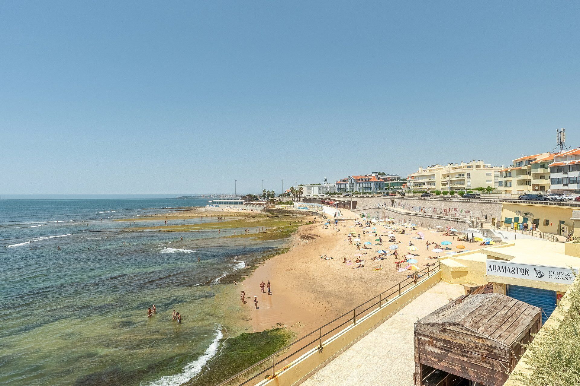A beach with clear waters, a sandy shore, and buildings in the background.