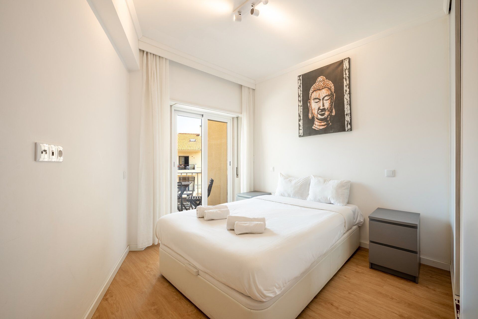Een hotelkamer met een bed, nachtkastjes, een schilderij en uitzicht door een geopende deur.