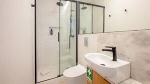 Un baño moderno con ducha de vidrio, inodoro blanco y lavamanos con dispensador de jabón.