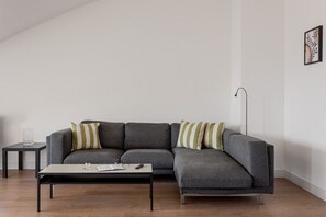 Ein modernes Wohnzimmer mit einem grauen Ecksofa, einem kleinen Beistelltisch und einer Stehlampe.
